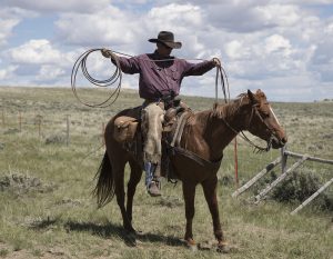 a man on a horse holding rope out, looping it into a lasso