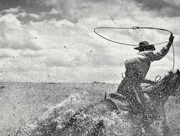 a man on horseback riding through water and lassoing a rope over his head