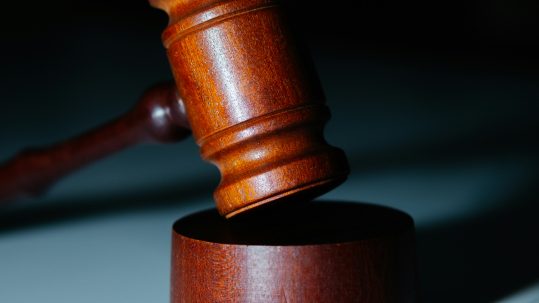 A wooden gavel rests on a block on a marble surface.