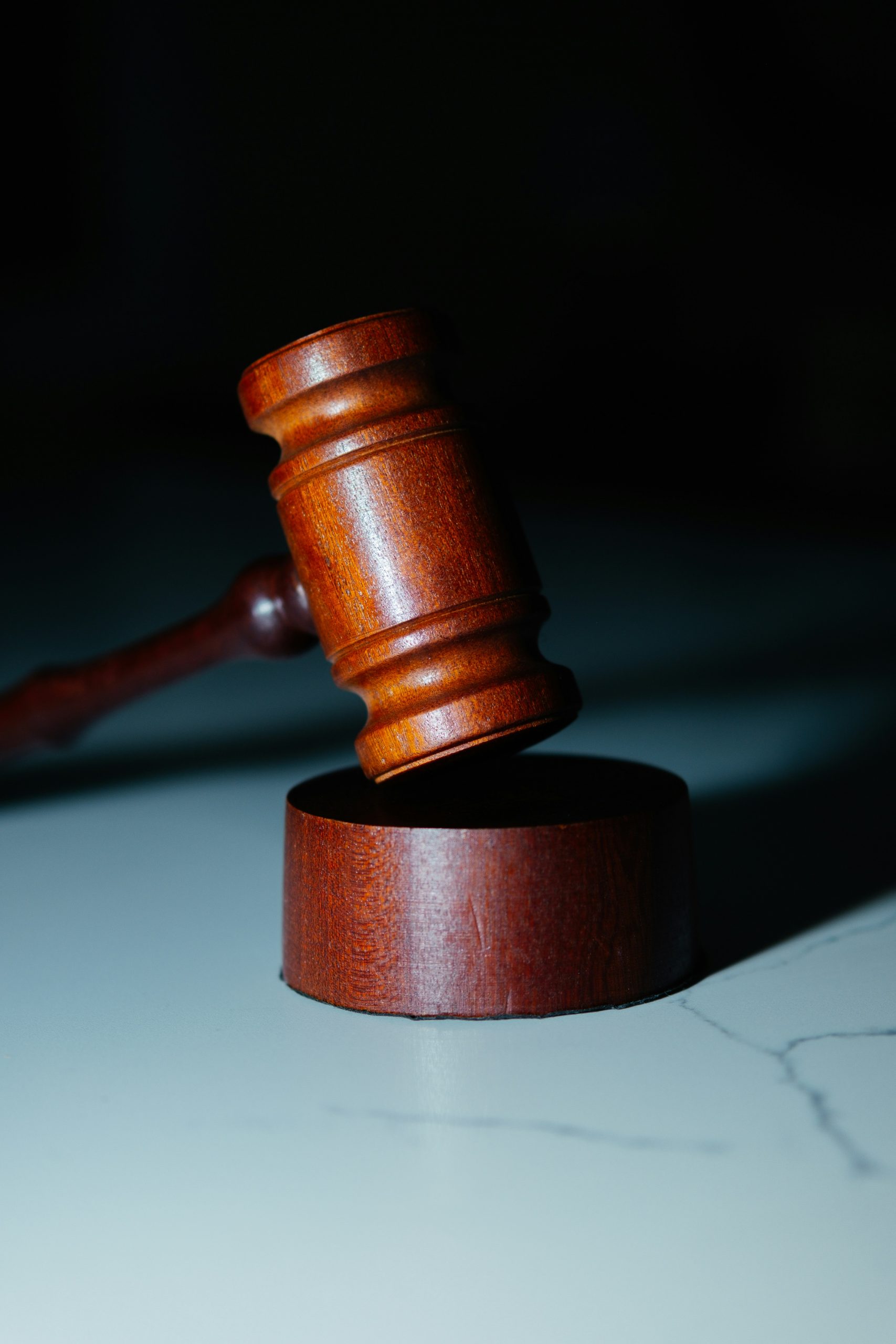 A wooden gavel rests on a block on a marble surface.