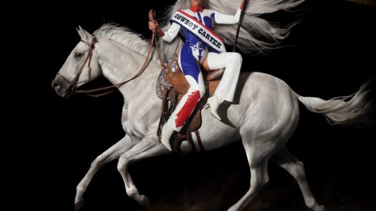 the album cover of Beyonce's Cowboy Carter. Beyonce sits on a white horse holding an American flag.